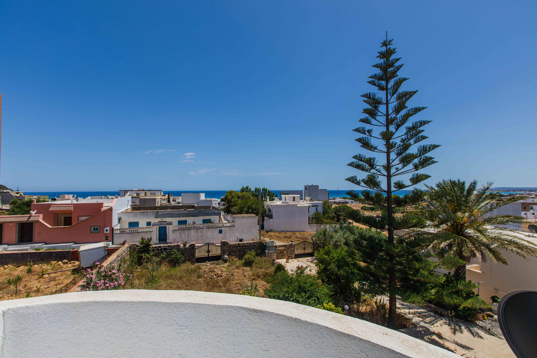 Vue dégagée sur des maisons blanches, arbres et mer bleue à l’horizon sous un ciel clair, El Haouaria (Cap Bon)